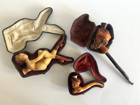 Pfeifenspitzen, Meerschaum, drei Stück mit einem Mundstück, um 1900. Fein gearbeitet, in Form eines vollplastischen männlichen Kopfes, eines weiblichen Kopfes sowie einer liegenden Dame. Mit originalen Formetuis.