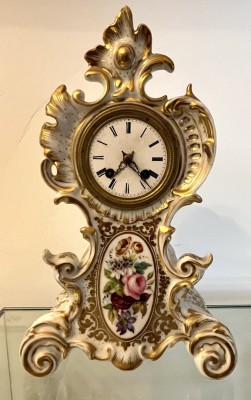 Porzellanuhr im Barockstil, um 1880, mit Goldstaffage und bunter Blumenbemalung. Emailliertes Zifferblatt und römische Ziffern. Mit Gang- und Schlagwerk, Funktion nicht geprüft. Mit Schlüssel.