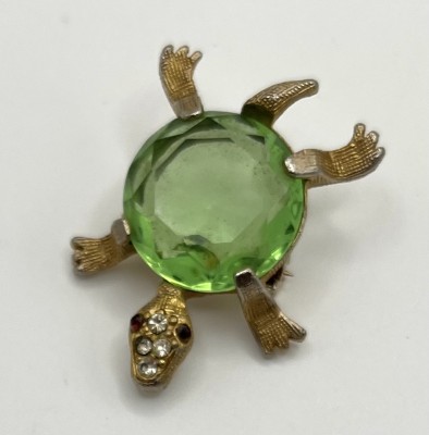 Brosche, in Form einer Schildkröte mit großem hellgrünen Saphir, vergoldet. Auf dem Kopf der Schildkröte die Augen als kleine Rubine und vier kleine Brillanten.