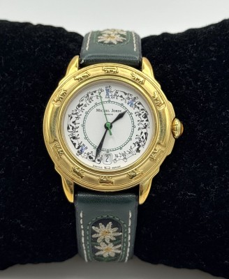 Michel Jordi Herrenarmbanduhr, Geneve, Quarzwerk. Datumsanzeige bei sechs Uhr, weißes Ziffernblatt mit ornamentaler Verzierung. Mit Edelweißapplikationen auf dem original Lederarmband, Funktion nicht geprüft.